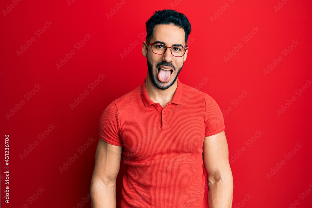 Young hispanic man wearing casual clothes and glasses sticking tongue out happy with funny expression. emotion concept.