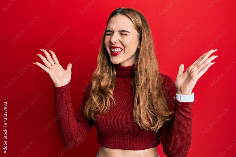 Young blonde woman wearing turtleneck sweater celebrating mad and crazy for success with arms raised and closed eyes screaming excited. winner concept Young blonde woman wearing turtleneck sweater celebrating mad and crazy for success with arms raised and closed eyes screaming excited. winner concept