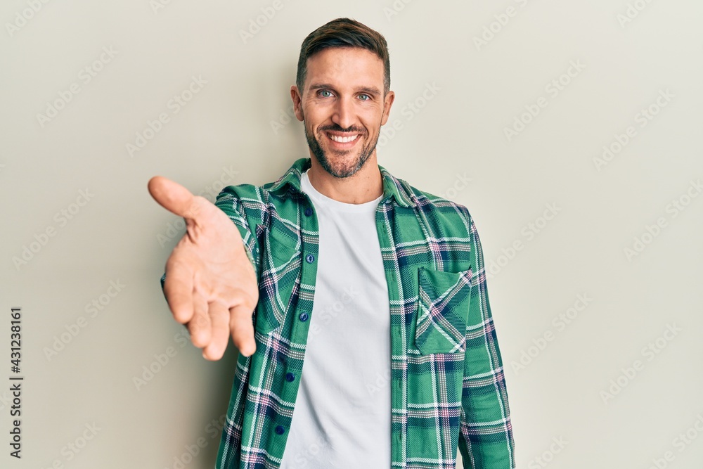 Handsome man with beard wearing casual clothes smiling friendly offering handshake as greeting and welcoming. successful business. Handsome man with beard wearing casual clothes smiling friendly offering handshake as greeting and welcoming. successful business.