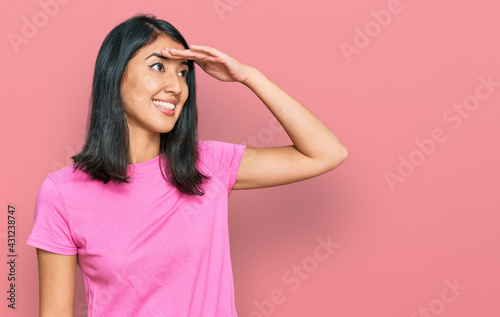 Beautiful asian young woman wearing casual pink t shirt very happy and smiling looking far away with hand over head. searching concept.