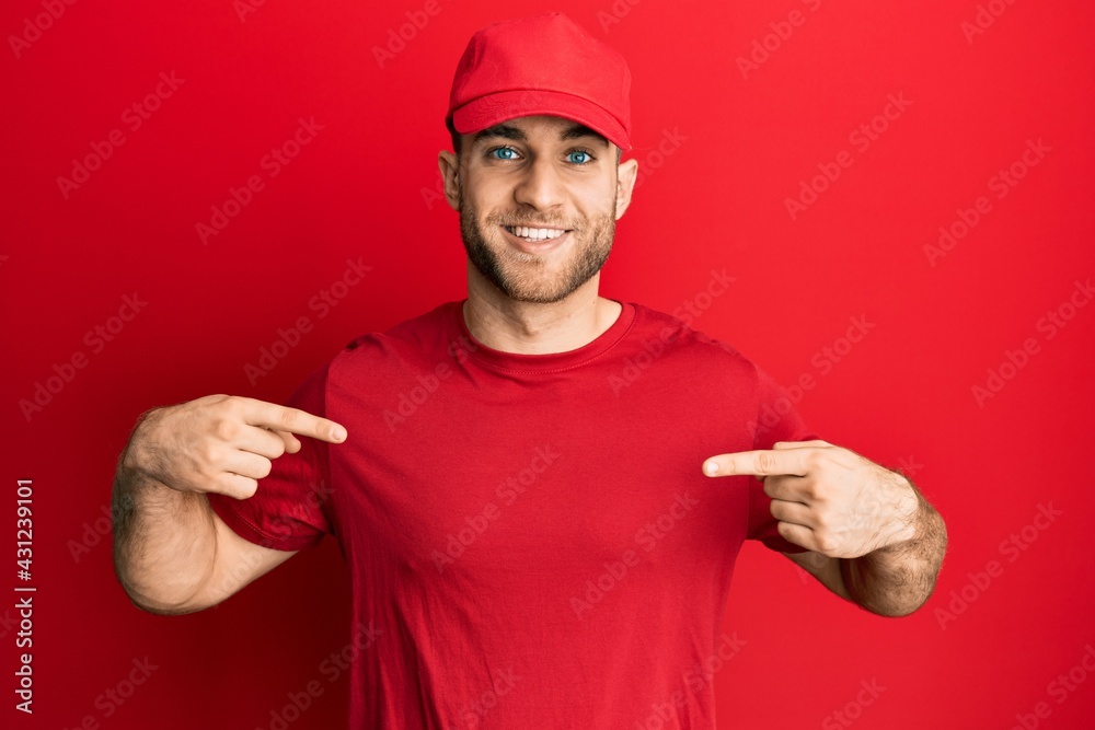Young caucasian man wearing delivery uniform and cap looking confident with smile on face, pointing oneself with fingers proud and happy.