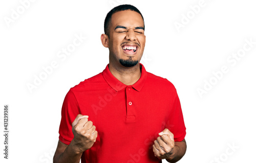 Young african american man wearing casual polo celebrating surprised and amazed for success with arms raised and eyes closed