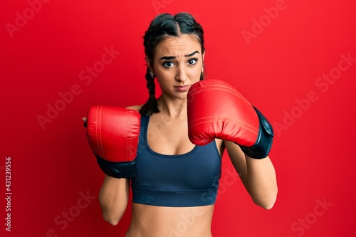 Young brunette girl using boxing gloves clueless and confused expression. doubt concept. © Krakenimages.com
