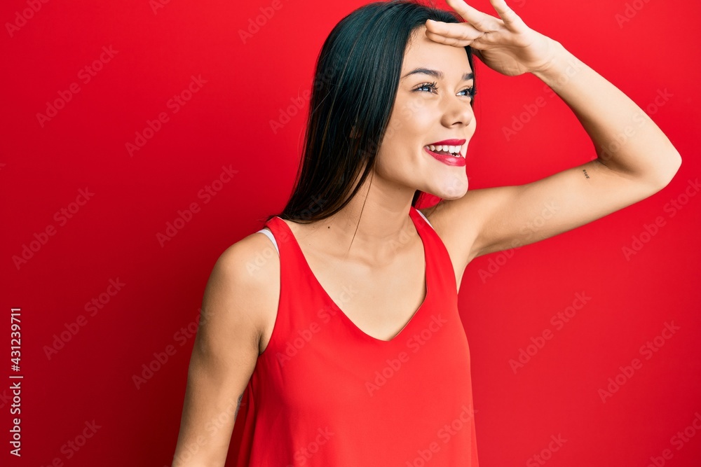 Young hispanic girl wearing casual style with sleeveless shirt very happy and smiling looking far away with hand over head. searching concept. Young hispanic girl wearing casual style with sleeveless shirt very happy and smiling looking far away with hand over head. searching concept.