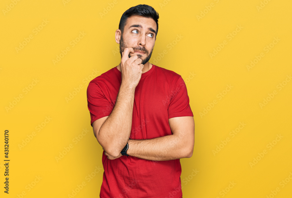 Young hispanic man wearing casual clothes serious face thinking about question with hand on chin, thoughtful about confusing idea Young hispanic man wearing casual clothes serious face thinking about question with hand on chin, thoughtful about confusing idea