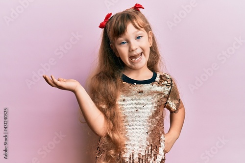 Foto Little caucasian girl kid wearing festive sequins dress smiling cheerful presenting and pointing with palm of hand looking at the camera