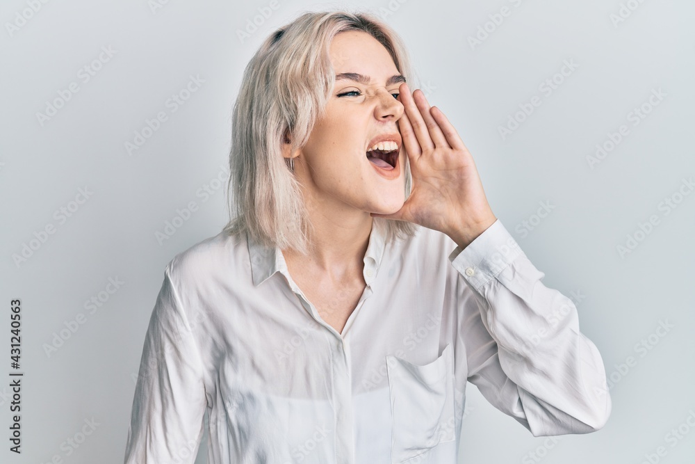 Young blonde girl wearing casual clothes shouting and screaming loud to side with hand on mouth. communication concept. Young blonde girl wearing casual clothes shouting and screaming loud to side with hand on mouth. communication concept.