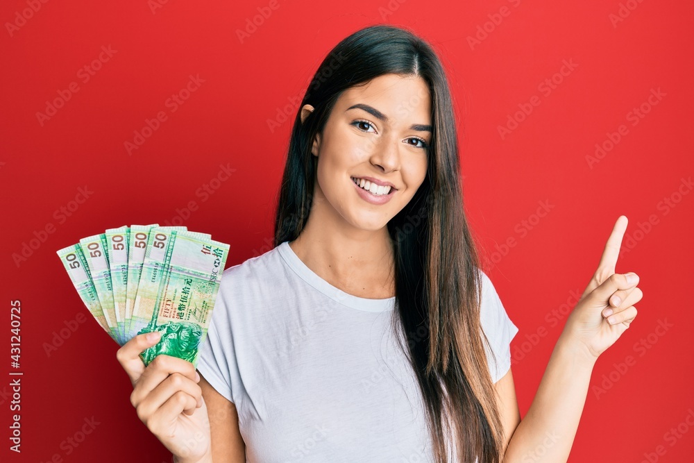 Young brunette woman holding hong kong 50 dollars banknotes smiling happy pointing with hand and finger to the side Young brunette woman holding hong kong 50 dollars banknotes smiling happy pointing with hand and finger to the side
