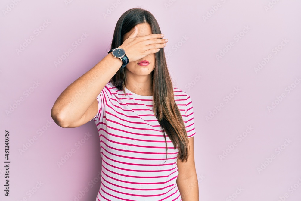 Young brunette woman wearing casual clothes over pink background covering eyes with hand, looking serious and sad. sightless, hiding and rejection concept Young brunette woman wearing casual clothes over pink background covering eyes with hand, looking serious and sad. sightless, hiding and rejection concept