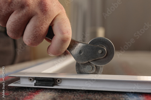 Man's hand with a wheel tool to install a aluminum mosquito screen. Horizontal image.