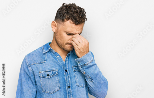 Young hispanic man wearing casual denim jacket tired rubbing nose and eyes feeling fatigue and headache. stress and frustration concept.