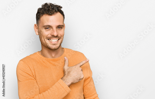 Young hispanic man wearing casual clothes cheerful with a smile of face pointing with hand and finger up to the side with happy and natural expression on face