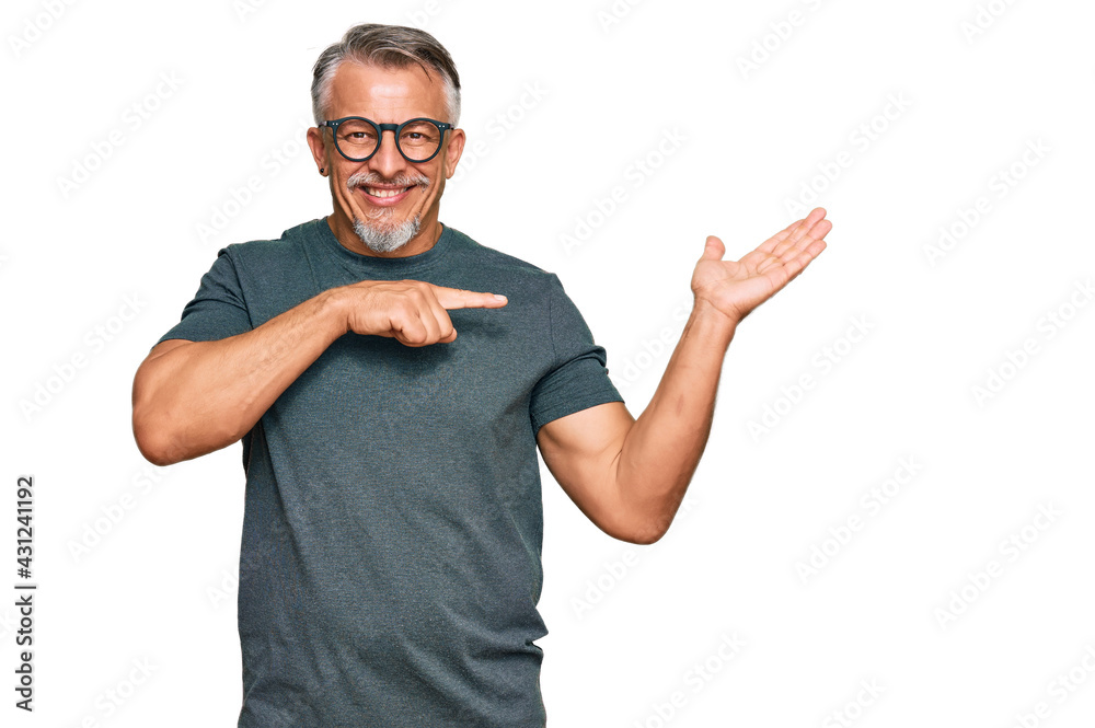 Middle age grey-haired man wearing casual clothes and glasses amazed and smiling to the camera while presenting with hand and pointing with finger. Middle age grey-haired man wearing casual clothes and glasses amazed and smiling to the camera while presenting with hand and pointing with finger.
