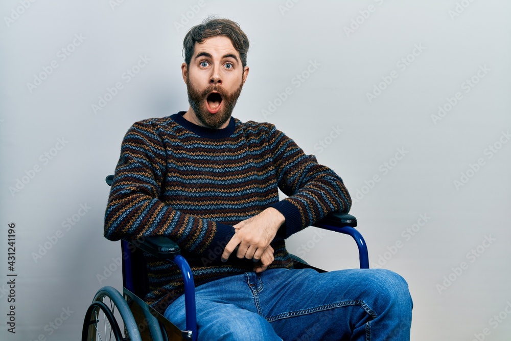 Caucasian man with beard sitting on wheelchair scared and amazed with open mouth for surprise, disbelief face Caucasian man with beard sitting on wheelchair scared and amazed with open mouth for surprise, disbelief face