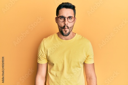 Young hispanic man wearing casual clothes and glasses making fish face with lips, crazy and comical gesture. funny expression.