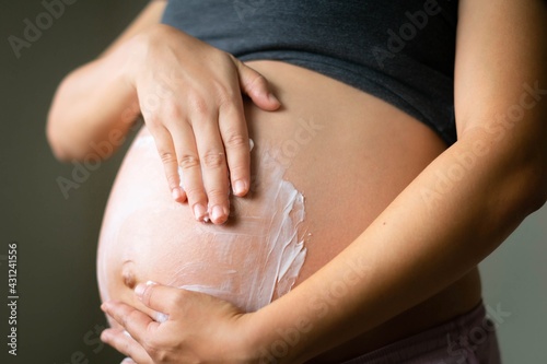 A pregnant woman massaging lotion on her baby belly. Prenatal skin care.