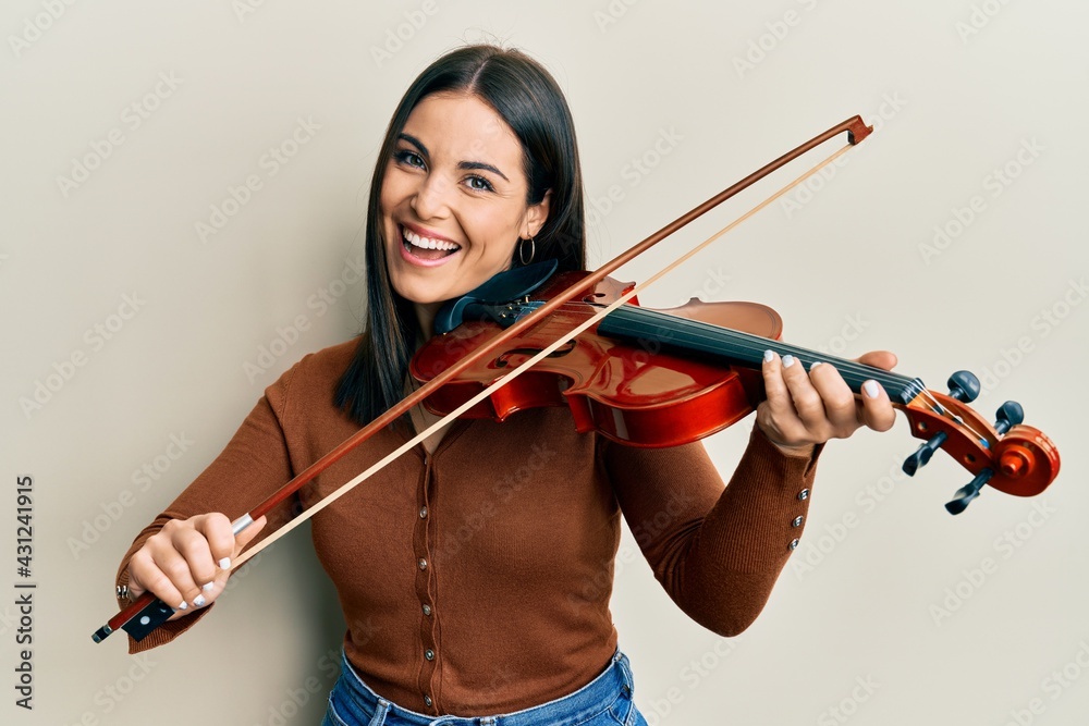 Young brunette woman playing violin smiling and laughing hard out loud because funny crazy joke. Young brunette woman playing violin smiling and laughing hard out loud because funny crazy joke.