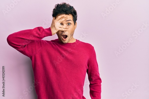 Handsome hispanic man wearing casual clothes over pink background peeking in shock covering face and eyes with hand, looking through fingers afraid