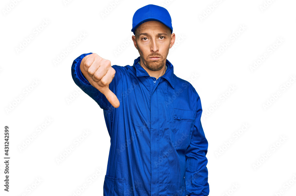 Bald man with beard wearing builder jumpsuit uniform looking unhappy and angry showing rejection and negative with thumbs down gesture. bad expression.