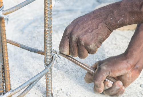 Dramatic image of Haitian construction worker tying rebar for concrete columns with weathered hands.