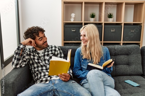 Young couple smiling happy reading book sitting on the sofa at home.