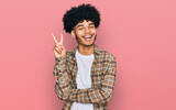 Young african american man with afro hair wearing casual clothes smiling with happy face winking at the camera doing victory sign. number two.