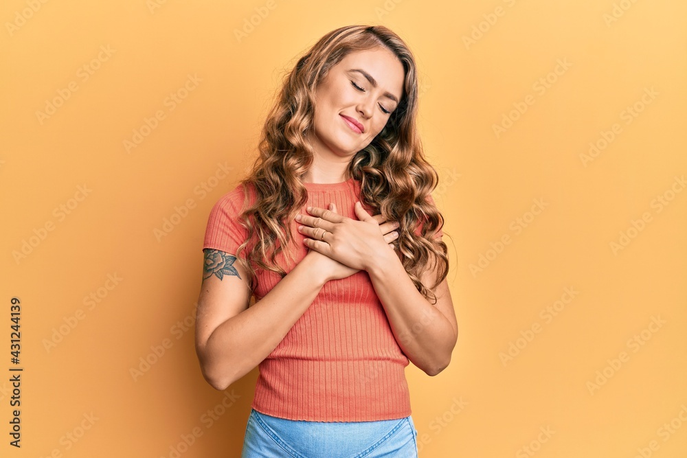 Young blonde girl wearing casual clothes smiling with hands on chest with closed eyes and grateful gesture on face. health concept. Young blonde girl wearing casual clothes smiling with hands on chest with closed eyes and grateful gesture on face. health concept.