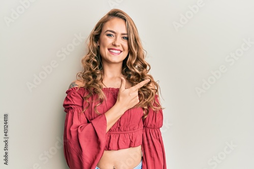 Young blonde girl wearing casual clothes smiling cheerful pointing with hand and finger up to the side