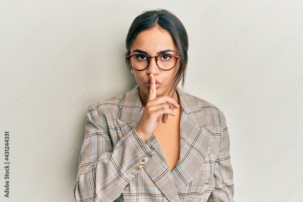 Young brunette woman wearing business jacket and glasses asking to be quiet with finger on lips. silence and secret concept. Young brunette woman wearing business jacket and glasses asking to be quiet with finger on lips. silence and secret concept.