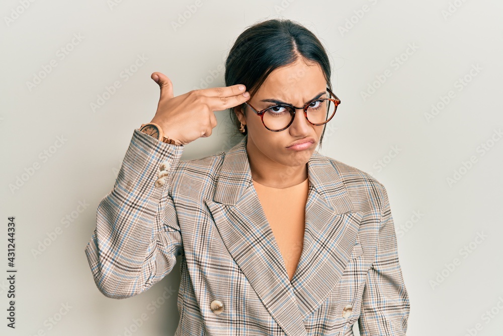 Young brunette woman wearing business jacket and glasses shooting and killing oneself pointing hand and fingers to head like gun, suicide gesture. Young brunette woman wearing business jacket and glasses shooting and killing oneself pointing hand and fingers to head like gun, suicide gesture.