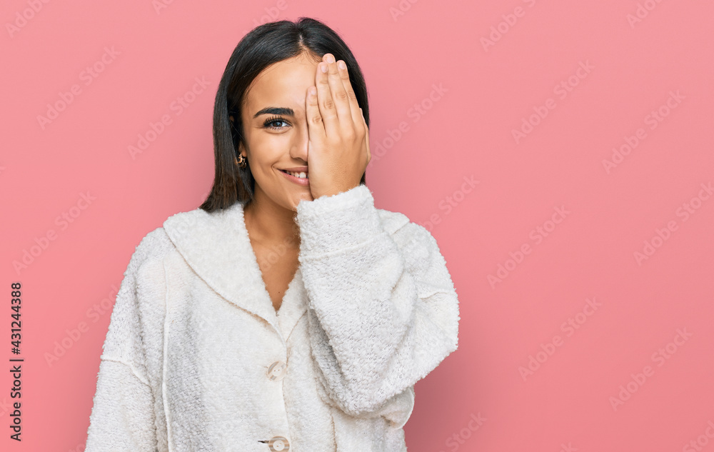 Young brunette woman wearing casual clothes covering one eye with hand, confident smile on face and surprise emotion. Young brunette woman wearing casual clothes covering one eye with hand, confident smile on face and surprise emotion.