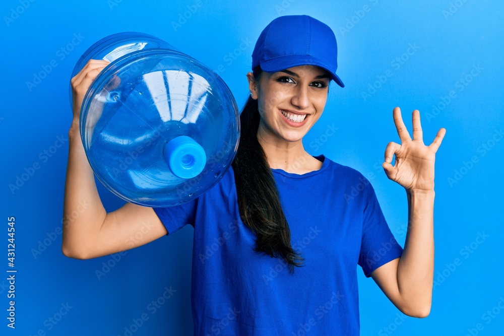 Young hispanic woman wearing delivery uniform holding water carafe doing ok sign with fingers, smiling friendly gesturing excellent symbol Young hispanic woman wearing delivery uniform holding water carafe doing ok sign with fingers, smiling friendly gesturing excellent symbol