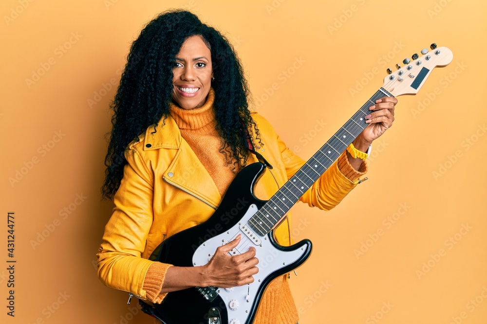 Middle age african american woman playing electric guitar smiling with a happy and cool smile on face. showing teeth. Middle age african american woman playing electric guitar smiling with a happy and cool smile on face. showing teeth.