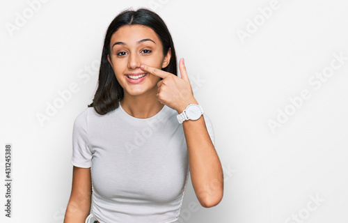 Young hispanic girl wearing casual white t shirt pointing with hand finger to face and nose, smiling cheerful. beauty concept