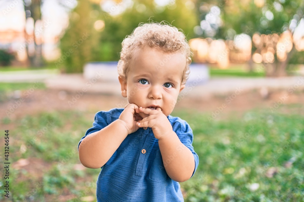 Sad little boy putting fingers on mouth touching gums because toothache at the park on a sunny day. Beautiful blonde hair male toddler in pain for new baby teeth outdoors Sad little boy putting fingers on mouth touching gums because toothache at the park on a sunny day. Beautiful blonde hair male toddler in pain for new baby teeth outdoors