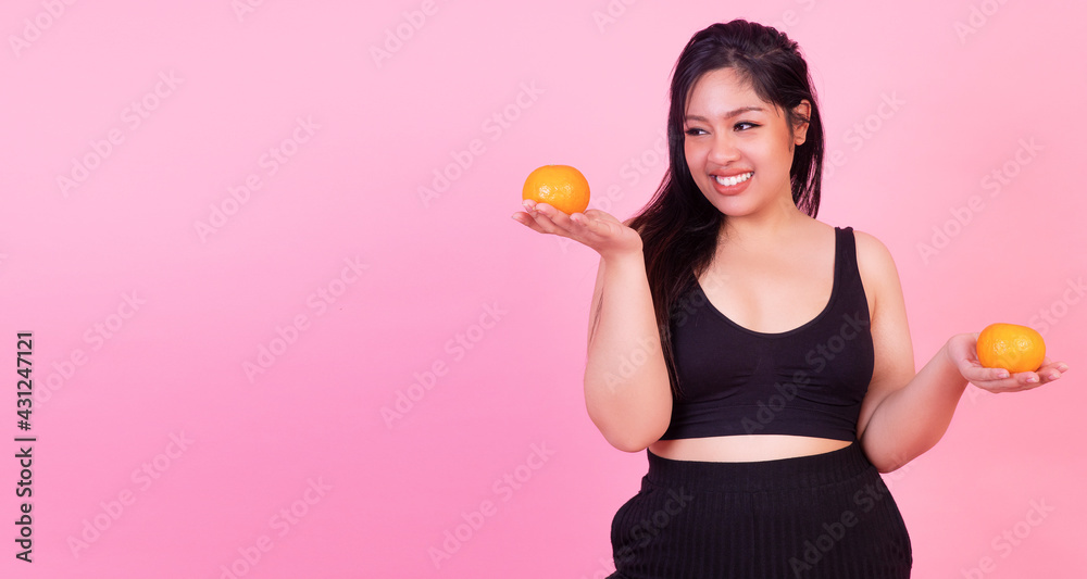 Weight loss concept. Overweight fat happy woman wearing sportswear holding fruits orange in hand while standing over isolated pink background. Chubby plus size girl dieting with fruit for body care. Weight loss concept. Overweight fat happy woman wearing sportswear holding fruits orange in hand while standing over isolated pink background. Chubby plus size girl dieting with fruit for body care.