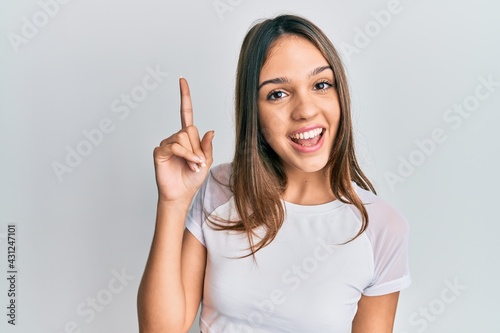 Young brunette woman wearing casual white t shirt smiling with an idea or question pointing finger up with happy face, number one