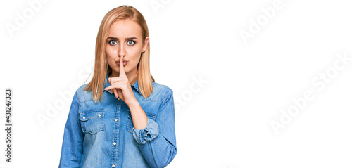 Beautiful caucasian woman wearing casual denim jacket asking to be quiet with finger on lips. silence and secret concept.