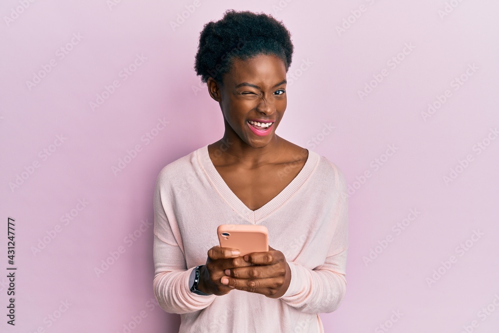 Young african american girl using smartphone winking looking at the camera with sexy expression, cheerful and happy face. Young african american girl using smartphone winking looking at the camera with sexy expression, cheerful and happy face.