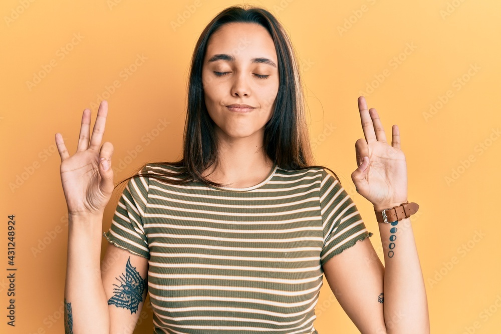 Young hispanic woman wearing casual striped t shirt relax and smiling with eyes closed doing meditation gesture with fingers. yoga concept. Young hispanic woman wearing casual striped t shirt relax and smiling with eyes closed doing meditation gesture with fingers. yoga concept.