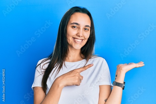Young hispanic woman wearing casual white t shirt amazed and smiling to the camera while presenting with hand and pointing with finger. © Krakenimages.com
