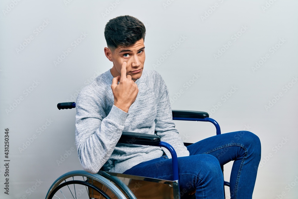 Young hispanic man sitting on wheelchair pointing to the eye watching you gesture, suspicious expression