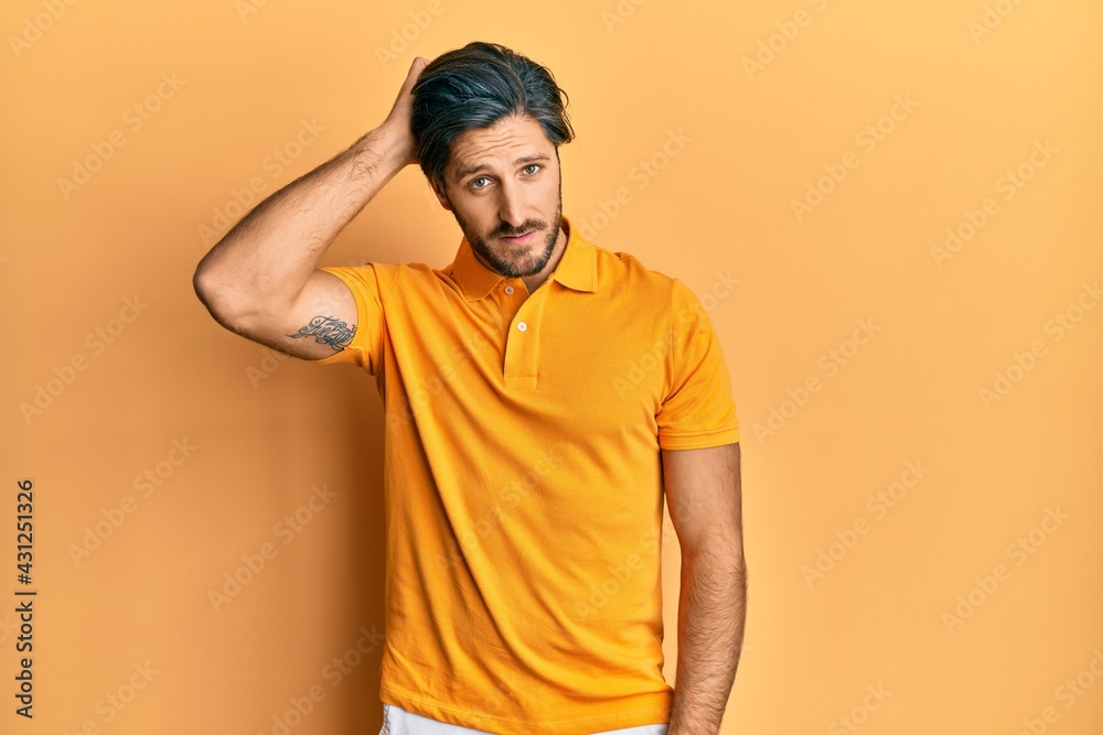 Young hispanic man wearing casual yellow t shirt confuse and wonder about question. uncertain with doubt, thinking with hand on head. pensive concept.