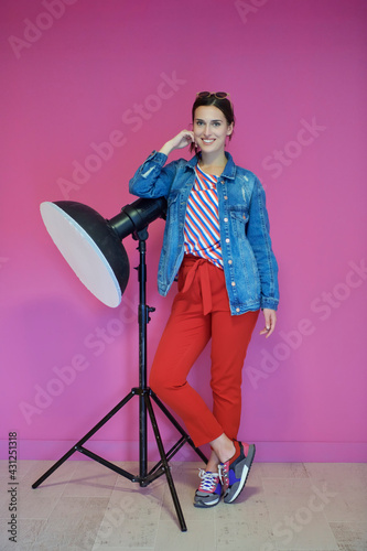 Young woman leaning against studio flashlight over a pink background