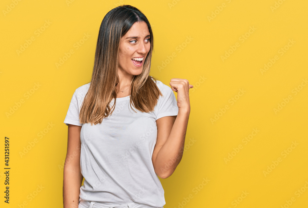 Young woman wearing casual white t shirt smiling with happy face looking and pointing to the side with thumb up. Young woman wearing casual white t shirt smiling with happy face looking and pointing to the side with thumb up.