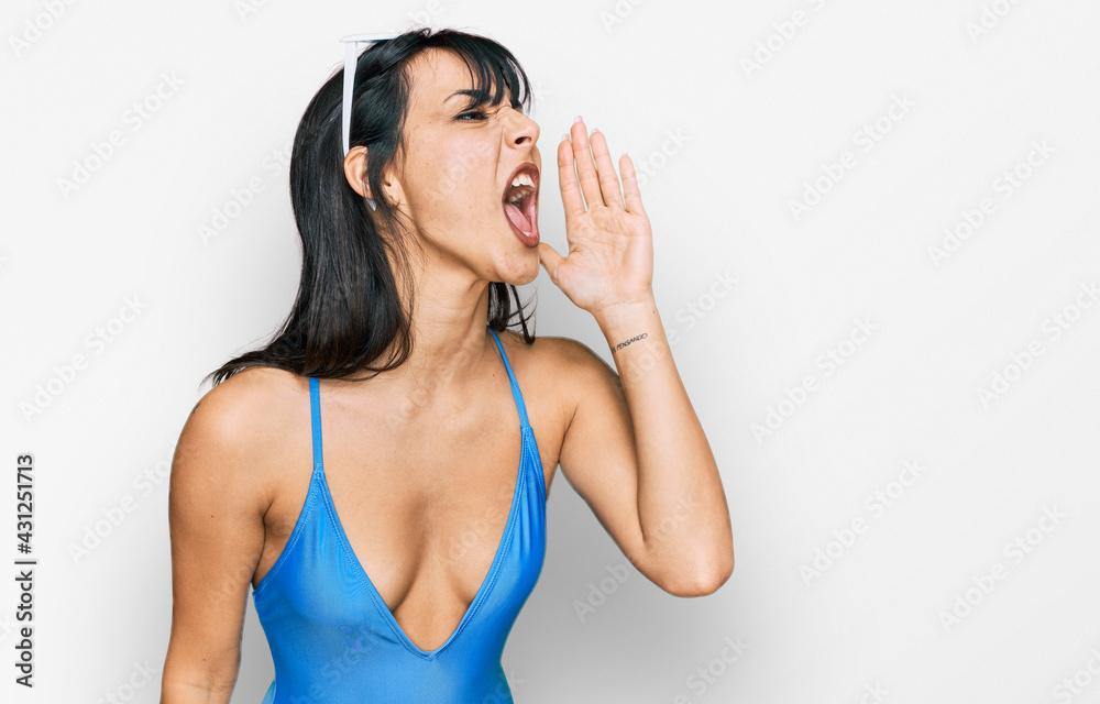 Young hispanic woman wearing swimsuit and sunglasses shouting and screaming loud to side with hand on mouth. communication concept. Young hispanic woman wearing swimsuit and sunglasses shouting and screaming loud to side with hand on mouth. communication concept.