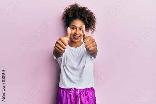 Beautiful african american woman with afro hair wearing sportswear approving doing positive gesture with hand  thumbs up smiling and happy for success. winner gesture.
