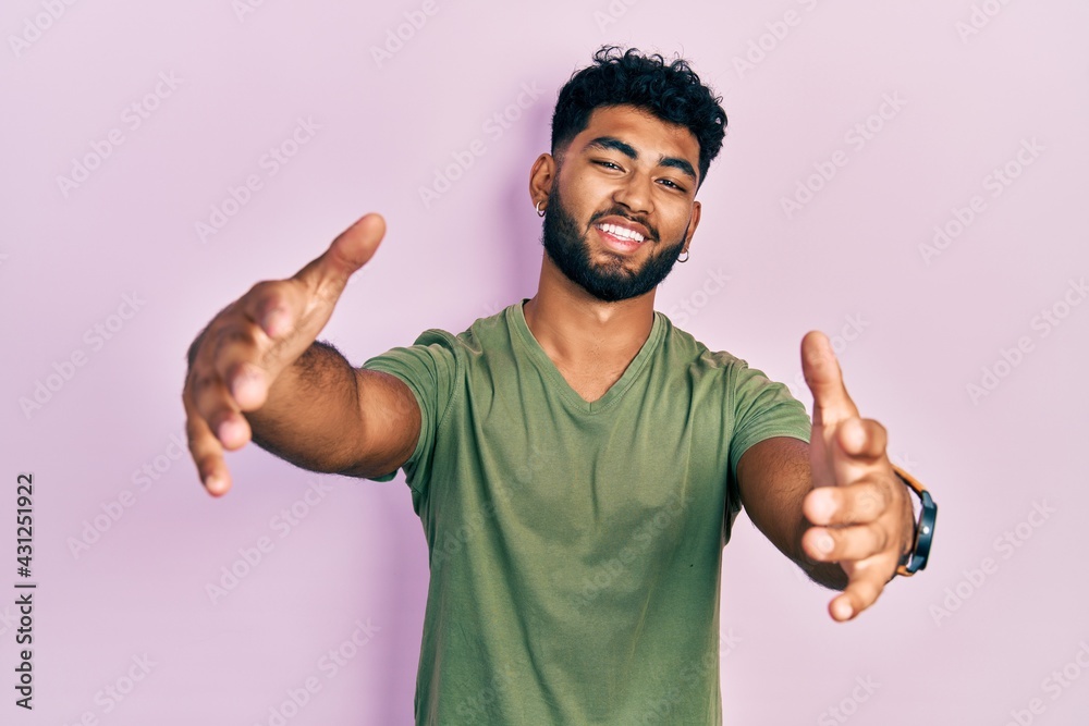 Arab man with beard wearing casual green t shirt looking at the camera smiling with open arms for hug. cheerful expression embracing happiness. Arab man with beard wearing casual green t shirt looking at the camera smiling with open arms for hug. cheerful expression embracing happiness.