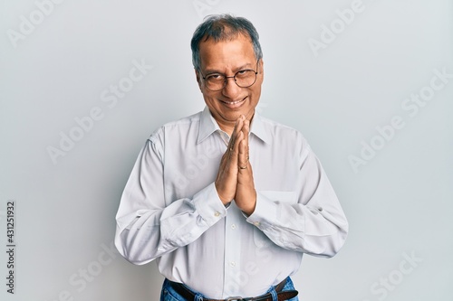 Middle age indian man wearing casual clothes and glasses praying with hands together asking for forgiveness smiling confident. © Krakenimages.com