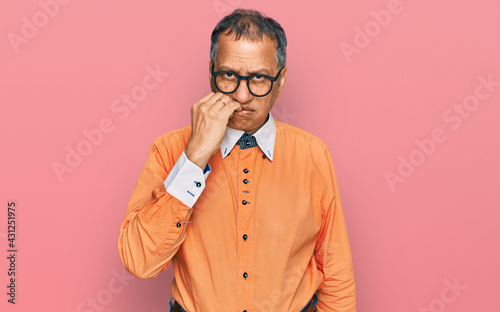 Middle age indian man wearing casual clothes and glasses looking stressed and nervous with hands on mouth biting nails. anxiety problem.